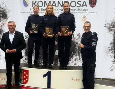 Trzy policjantki stoją na podium z numerem 1, trzymając pamiątkowe tablice z odznakami i sztyletami, podczas uroczystości wręczenia nagród na zawodach Komandosa